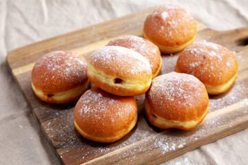 Homemade Apricot Polish Paczki Donut with Powdered Sugar on a Wooden Board, side view.