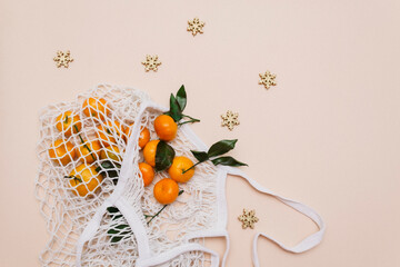 Top view of a white grocery eco-mesh cotton bag with fresh orange tangerines on a beige pastel...