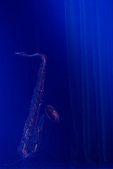 A saxophone on stage in moody blue lighting with beams of light cutting across it just before the...