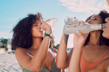 Beach, friends and African women drink bottle of liquid cold drink to relax on Summer vacation in...