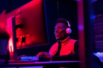 Young African man playing video game on the computer. Streamer guy sitting at home and playing another match.