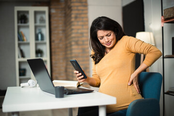 Fototapeta premium Young pregnant woman having painful contraction. Businesswoman holding her belly.