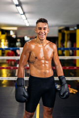 Fototapeta na wymiar Portrait of a young muscular kickboxer with gloves on looking at camera and smiling standing on the ring