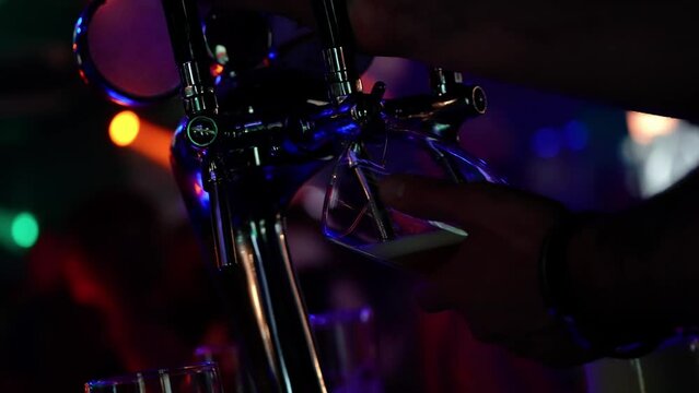 Alcoholic beverages, bartender pours beer into a glass, night club party, multicolored light.