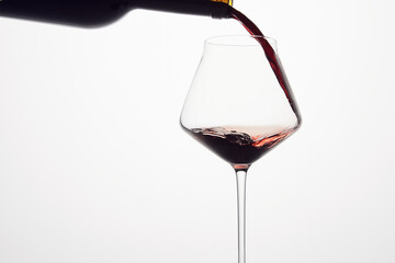 Red wine is poured from bottle into transparent glass.