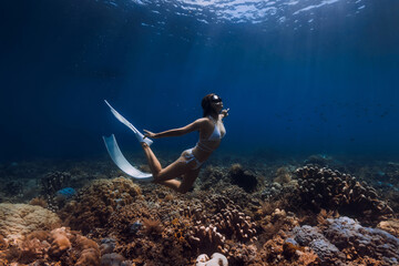 Free diver woman glides with fins over corals. Freediving in deep blue ocean
