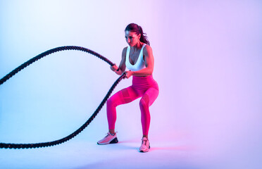 Artistic image with colored gel lights of a beautiful fit woman making exercises in the gym with...