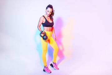 Fototapeta na wymiar Artistic image with colored gel lights of a beautiful fit woman making exercises in the gym with sport equipments and gear