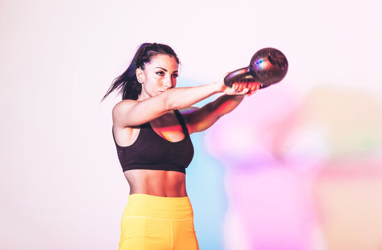 Artistic image with colored gel lights of a beautiful fit woman making exercises in the gym with sport equipments and gear