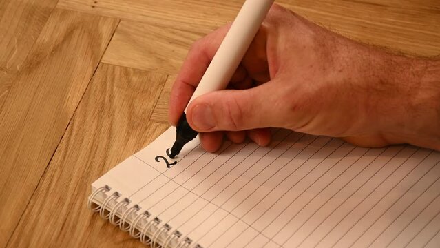 A person is writing by hand an action plan to get started on 2023 written with a black marker on a lined writing pad. 
