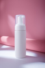 White bottle with dispenser mockup on pink backdrop in harsh light, no brand template. Cleansing facial foam container with paper decor