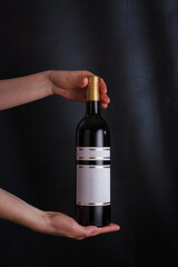 hands holding bottle of red wine with mock up label, no brand on black background. Cabernet sauvignon, merlot, pinot noir. Alcohol drink, copy space