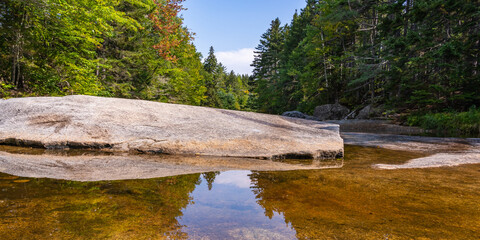A smooth, glacier-cut boulder across the Ammonoosuk River, surrounded by forests in the foothills of Mount Washington in New Hampshire's White Mountain National Forest.