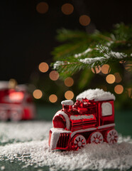 Christmas decorations red train in the snow with branch of Christmas tree with beautiful bokeh light on dark background, selective focus. New Year's train