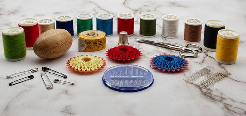 Sewing tools and accessories: scissors, tape measure, spools of thread, needle, thimble and pins isolated on marble background.