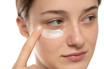 Beauty young smiling woman applying cosmetic cream under her eye on a white background