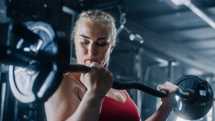 Fototapeta na wymiar A Motivated Athlete Training with Barbell and Heavy Weights. Female Professional Bodybuilder Sweating While Doing her Workout Routine at the Gym. She Is Looking at her Arms While Exercising.