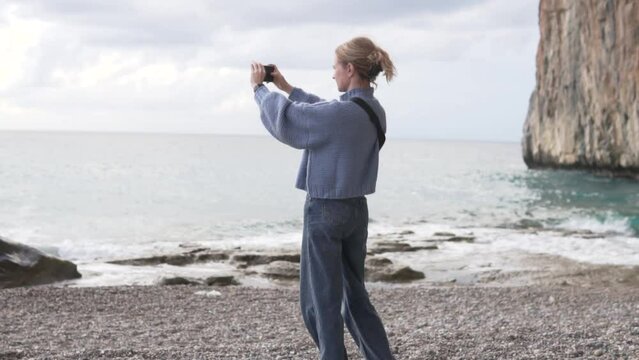 A tourist woman takes a photo of the sea in a beautiful place near a cliff.
