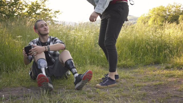 Young disabled man sitting in nature with friend, talking.