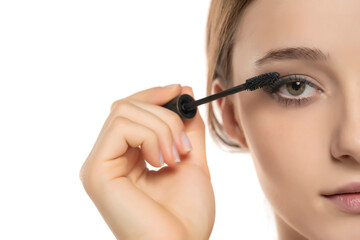 Fototapeta premium Half portrait of a young woman applying mascara with brush on a white studio background
