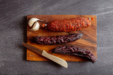 Three sausages and a knife on a wooden cutting board. Overhead view.