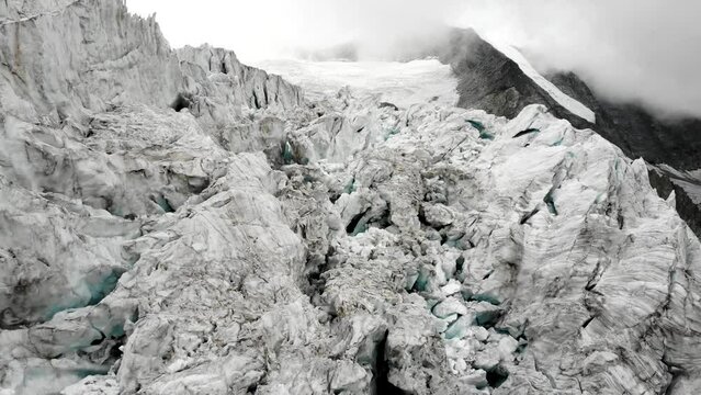 Aerial flyover through the crevasses of the Moiry glacier near Grimentz in Valais, Switzerland with a pan down view from the mountain peaks to the ice on a cloudy summer afternoon