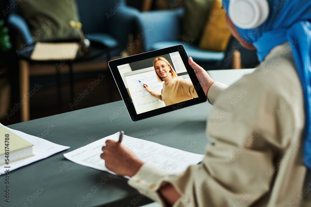 Poster focus on tablet screen with blond confident teacher pointing at whiteboard during explanation of eng
