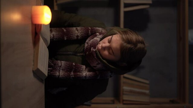 An angry student warmly dressed, feeling cold at home, studying by candlelight, poor woman unable to pay for electricity. No heating, electric crisis in Europe