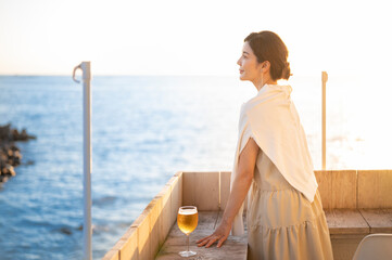 夕暮れ時、海を眺めながらビールを飲む女性
