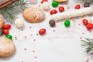 Fototapeta na wymiar candies and cookies with christmas tree branches on white marble background