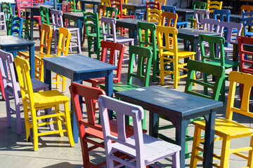 Fototapeta na wymiar Street cafe in summer with color wooden vintage chairs and tables on a tourist street. Colored furniture and cafe design