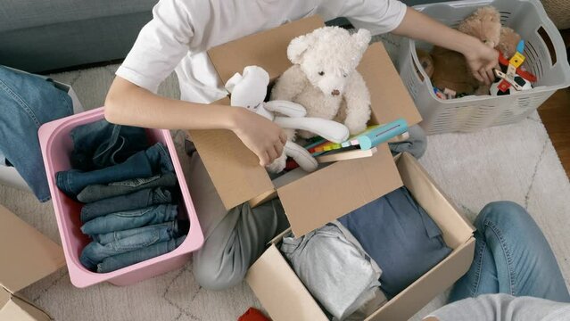 Woman and child sorting old clothes, toys and packing into cardboard boxes. Donations for charity, help low income families, declutter home, moving moving into new home, recycling, sustainable living