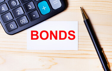On a light wooden background, a black calculator, a pen and a business card with the text BONDS