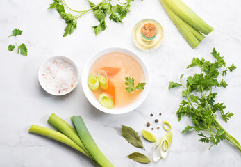 Basic bone broth in a bowl with parsley, leek, bay leaf and black pepper on a white background. Winter base for hot recipes - soups, risottos, pastas and sauces. Top view