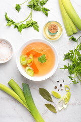 Basic vegetarian broth in a white bowl with parsley, leek, bay leaf and black pepper on a white background. Winter base for hot recipes: soups, risottos, pastas and sauces. Front view