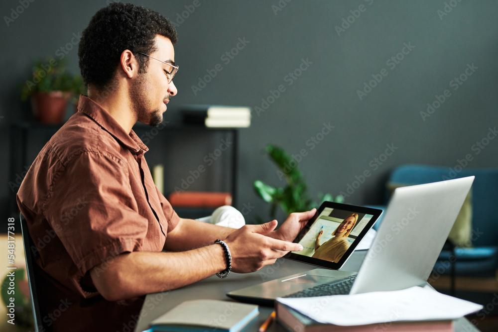 Poster young confident man looking at teacher making presentation on tablet screen and discussing points of