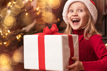 Fototapeta na wymiar Christmas Child Little Girl with Christmas Gift Box on Christmas Lights Background. Happy, Amazed, Surprised Kid Receiving Christmas Present or Gift. Christmas Holiday.
