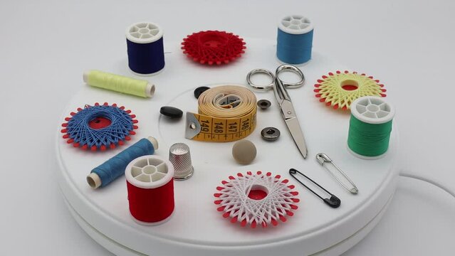 Sewing tools and accessories: scissors, tape measure, spools of thread, thimble and pins rotating isolated on white background. Video in 4k