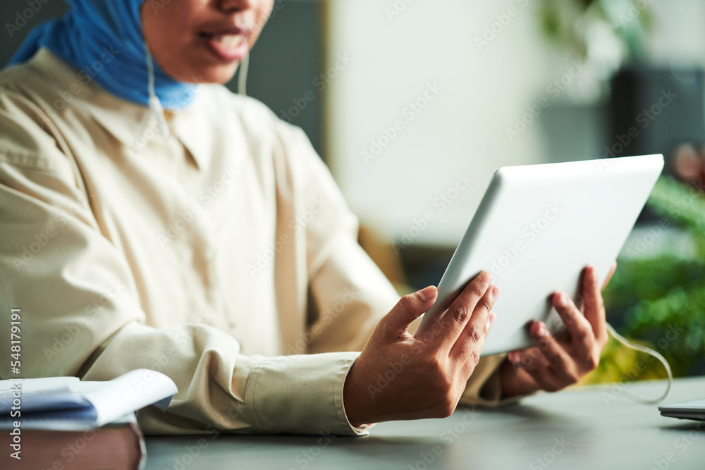 Poster hands of young muslim tutor holding tablet in front of herself while communicating with online stude