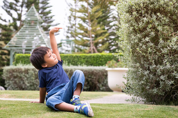 Fototapeta premium Adorable asian boy sitting in the garden and point to somewhere. Happy asian toddler child.