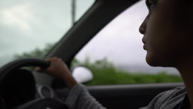 Close-up of young Asian woman driving car confidently with calm face, side angle shot