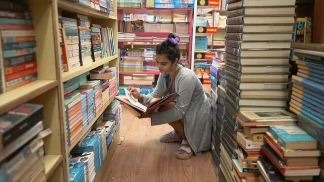 Beautiful young Asian girl sitting in the middle of bookshelves and reading, Side angle tracking in shot