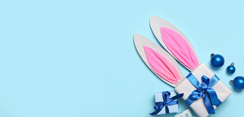 Paper bunny ears with Christmas balls and gifts on light blue background with space for text