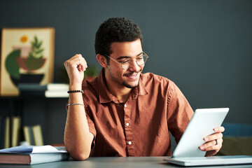 Young smiling male student of online course of study looking at tablet screen while sitting by desk and watching video lesson