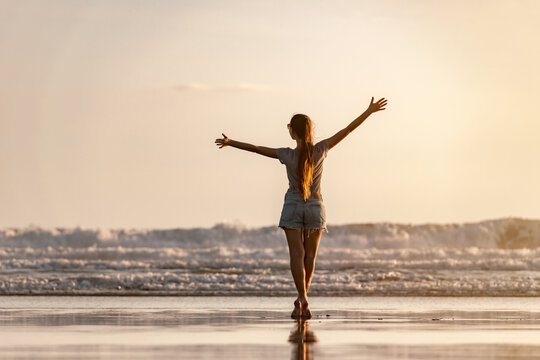 Happy young girl is standing with open arms at sunset sea beach