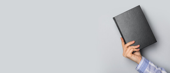 Hand holding black book on grey background with space for text