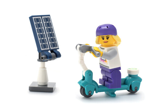 Lego minifigure of girl on electro scooter. Editorial illustrative image of usage of solar panel or photovoltaic as green energy and alternative power source.