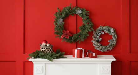 Beautiful Christmas wreaths hanging on red wall near fireplace in room