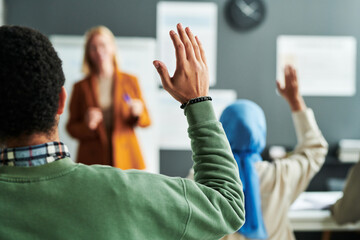 Part of back of young male student in green pullover raising hand at lesson to ask question to teacher or give his answer - obrazy, fototapety, plakaty