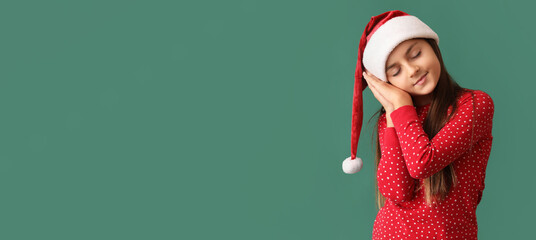 Cute sleepy girl in pajamas and Santa hat on green background with space for text